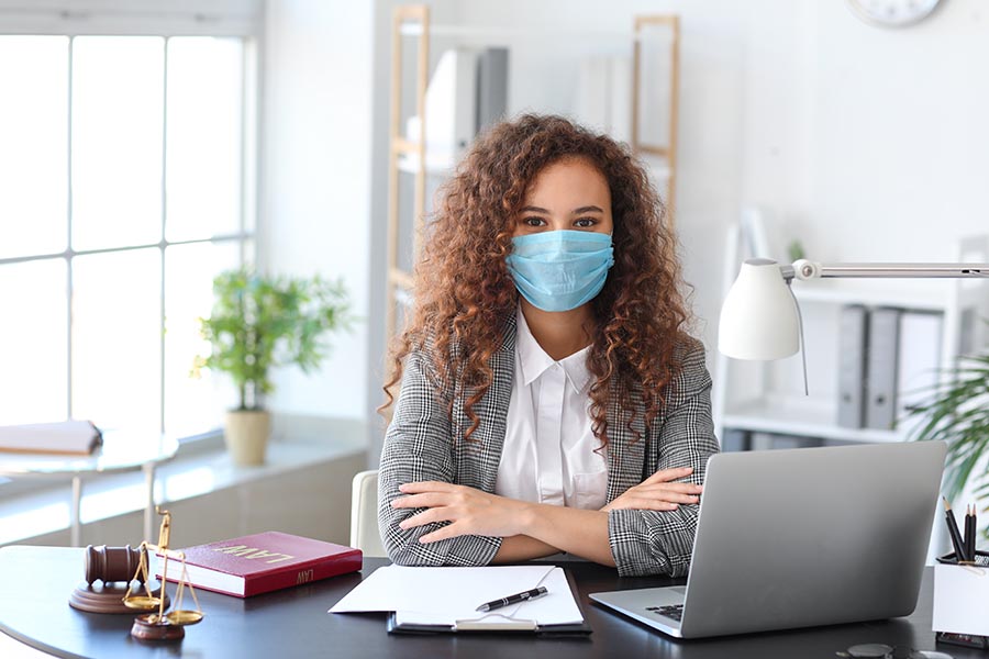 COVID-19 Information - Businesswoman at a Desk With Computer Wearing a Mask in Modern Office